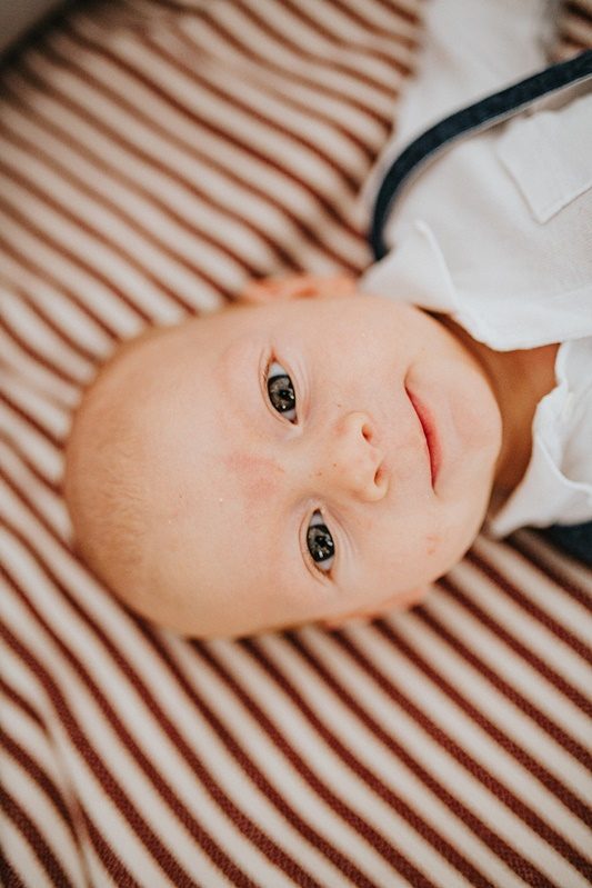 Portrait de bébé allongé sur un lit rayé — séance naissance ANtO photographe