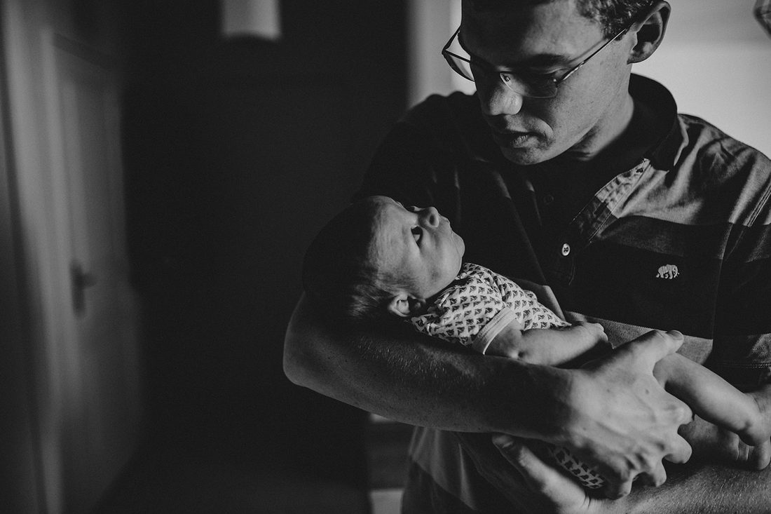 Père observant son nouveau-né dans ses bras, instant suspendu — séance naissance ANtO photographe