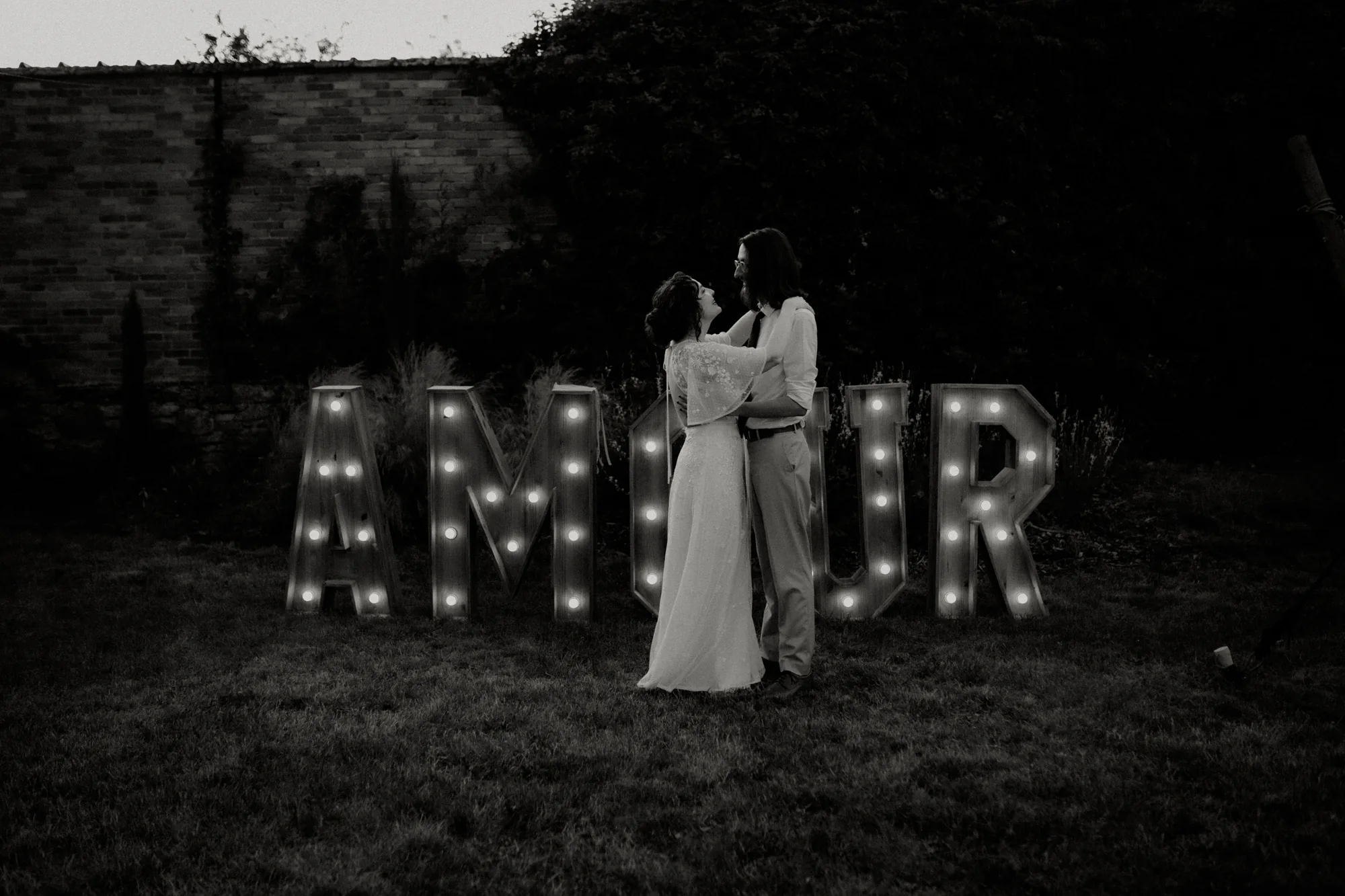 Mariés enlacés devant l'enseigne lumineuse AMOUR à la tombée de la nuit — mariage Thiers Clermont-Ferrand, ANtO photographe