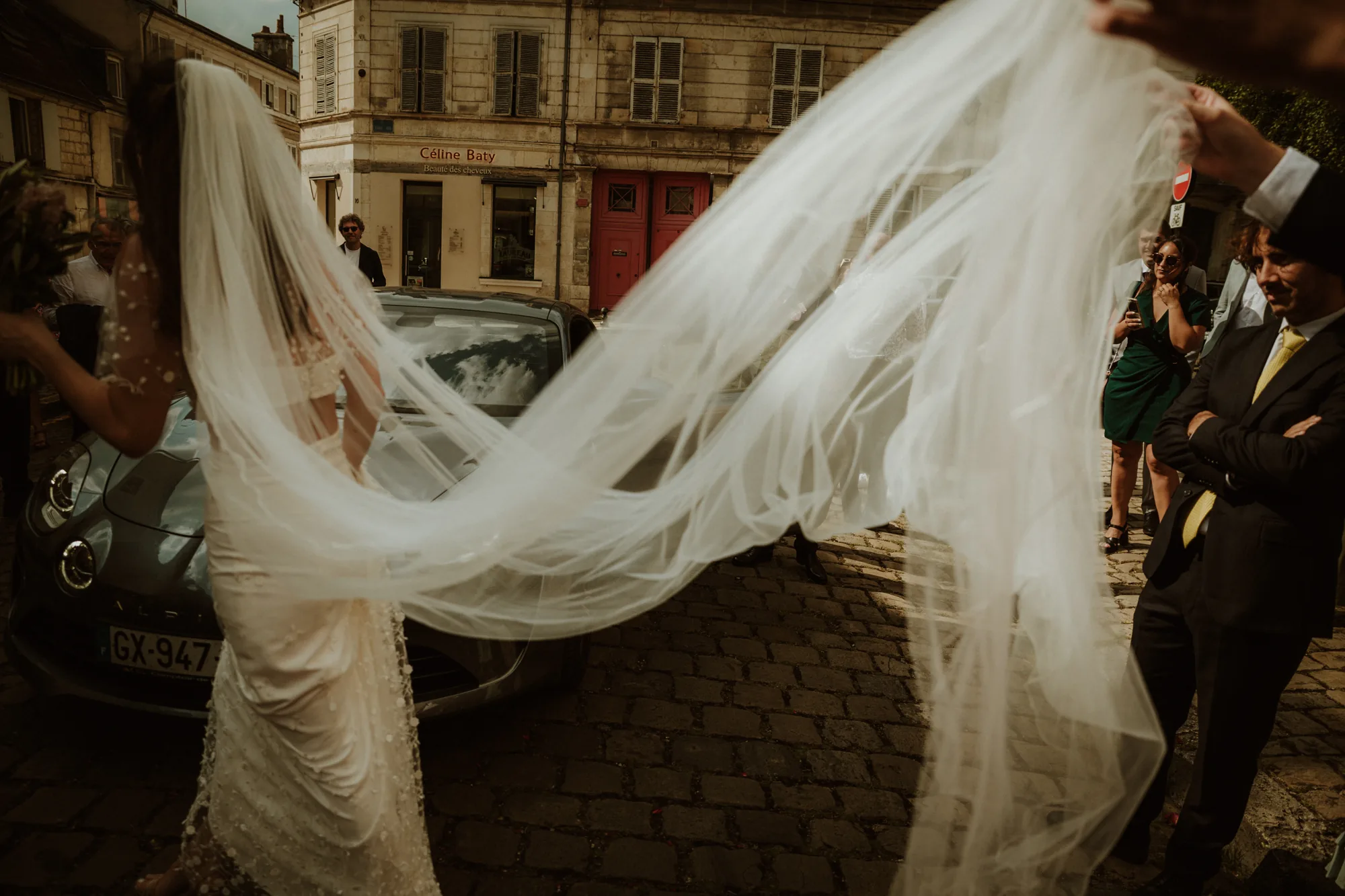 Voile de la mariée s'envolant devant une voiture ancienne, rue pavée — mariage Thiers Clermont-Ferrand, ANtO photographe